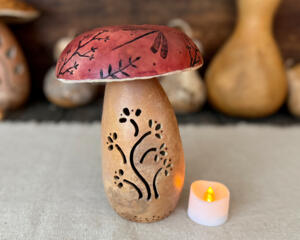 Decorative mushroom made from dried gourds. A berry color top has dragonfly artwork. The bottom as a carved vine that lights with a candle. 